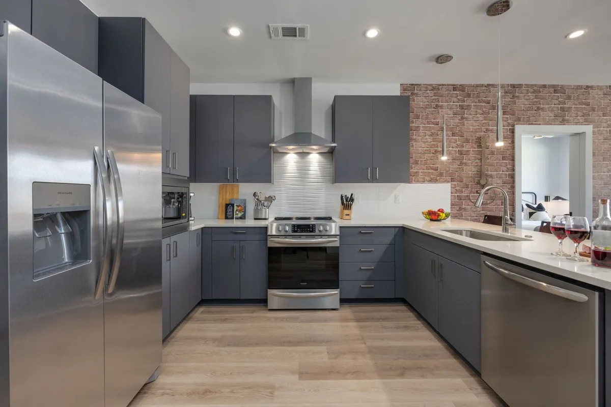 A contemporary kitchen with a stainless steel refrigerator, kitchen island, modern stove and oven, brick accent wall, and pendant lighting. The island features bar stools, ideal for both dining and socializing while cooking.