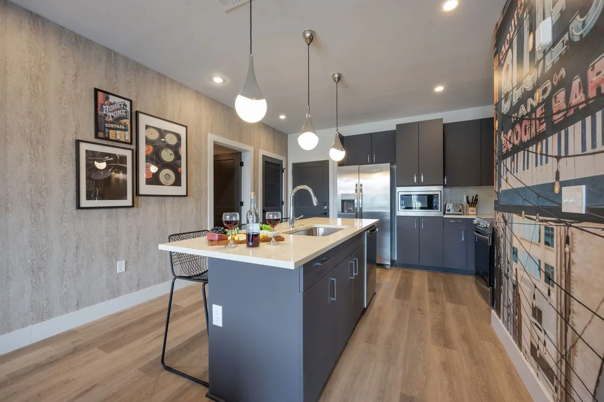 A sleek, modern kitchen with an island, surrounded by contemporary appliances and vibrant wall art. The open layout encourages socializing and easy access for snacks or drinks during group gatherings.