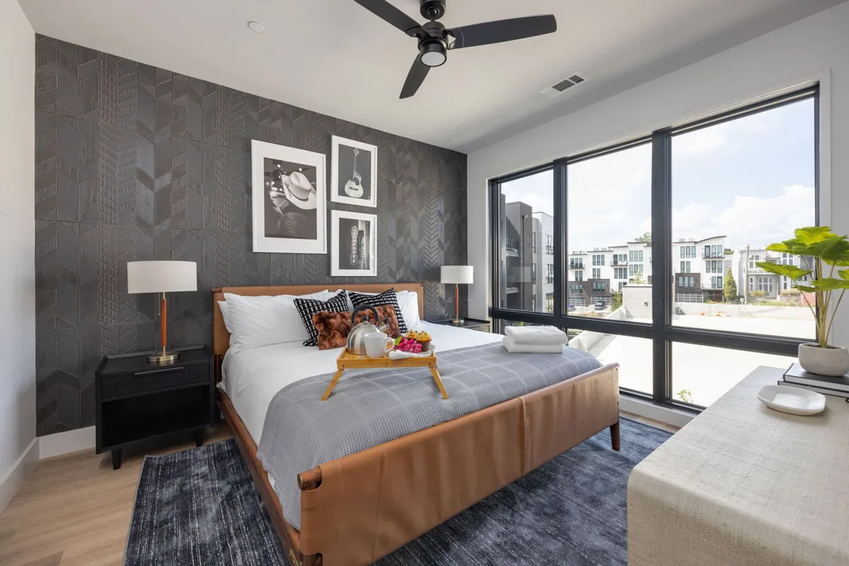 This modern bedroom features a stylish headboard, decorative pillows, large windows for ample natural light, and contemporary artwork. The atmosphere feels restful and updated—ideal for secondary bedrooms or additional sleeping spaces.