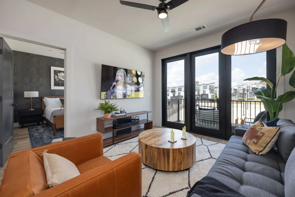 A contemporary living space with a large television displaying a live performance, a round wooden coffee table, and a mix of comfortable seating. The setup encourages communal activities like watching shows or hosting movie nights.