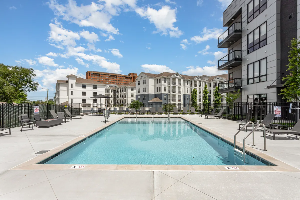 A stylish swimming pool area with lounge chairs and surrounding buildings, suggesting a relaxed environment for guests to enjoy after a productive day. The scene is tranquil, offering both leisure and a sense of modern amenities.