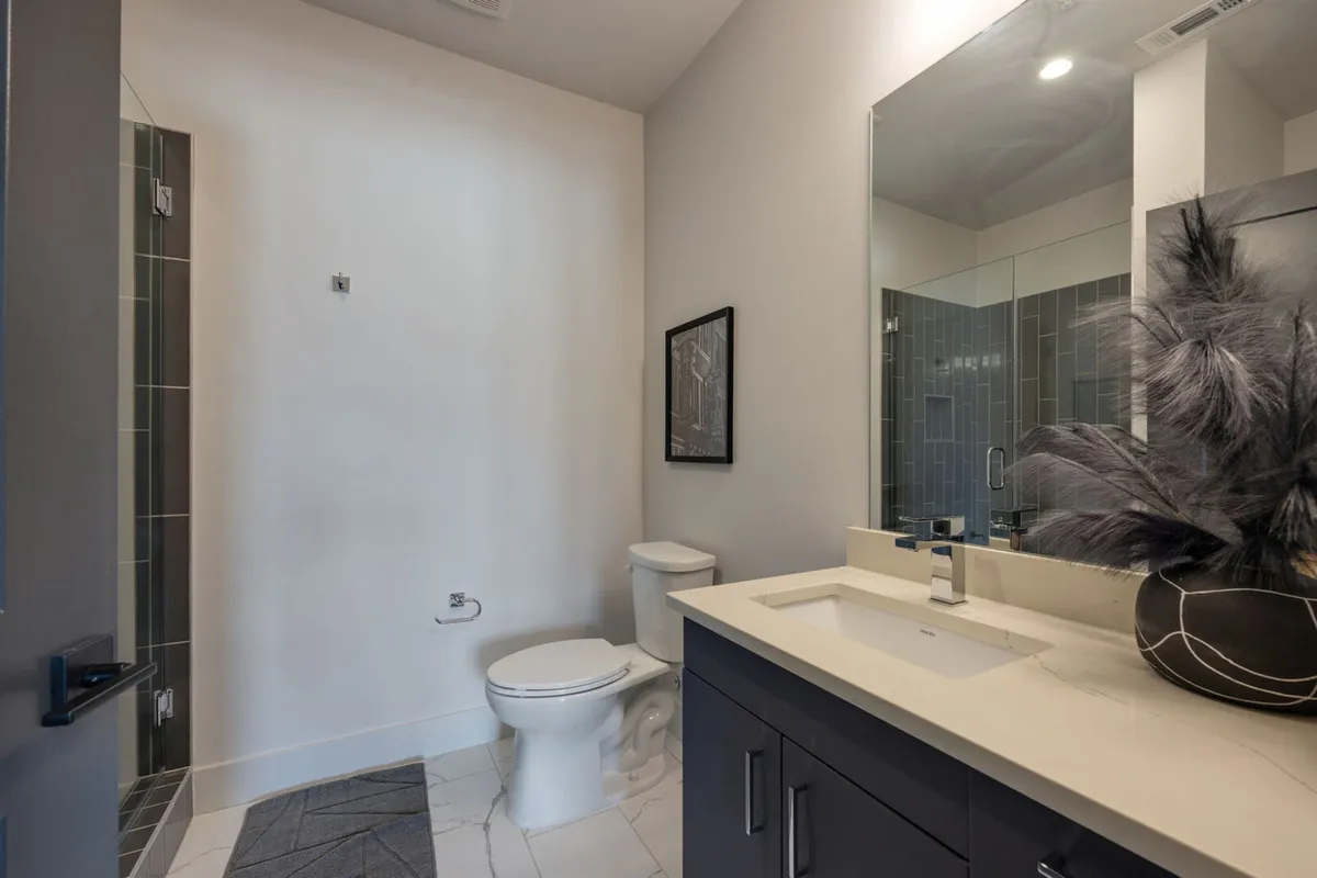 A spacious, contemporary en-suite bathroom is displayed here, with a large vanity, ample mirror, decorative plant, and glass-enclosed shower. The design supports both relaxation and daily routines.